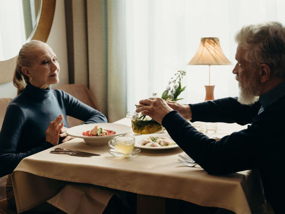 Two older adults sharing a meal at a lamp-lit dining table